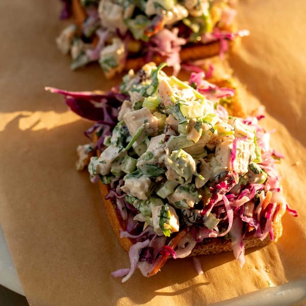 Two open-faced sandwiches with chicken salad and red cabbage slaw on toasted bread.