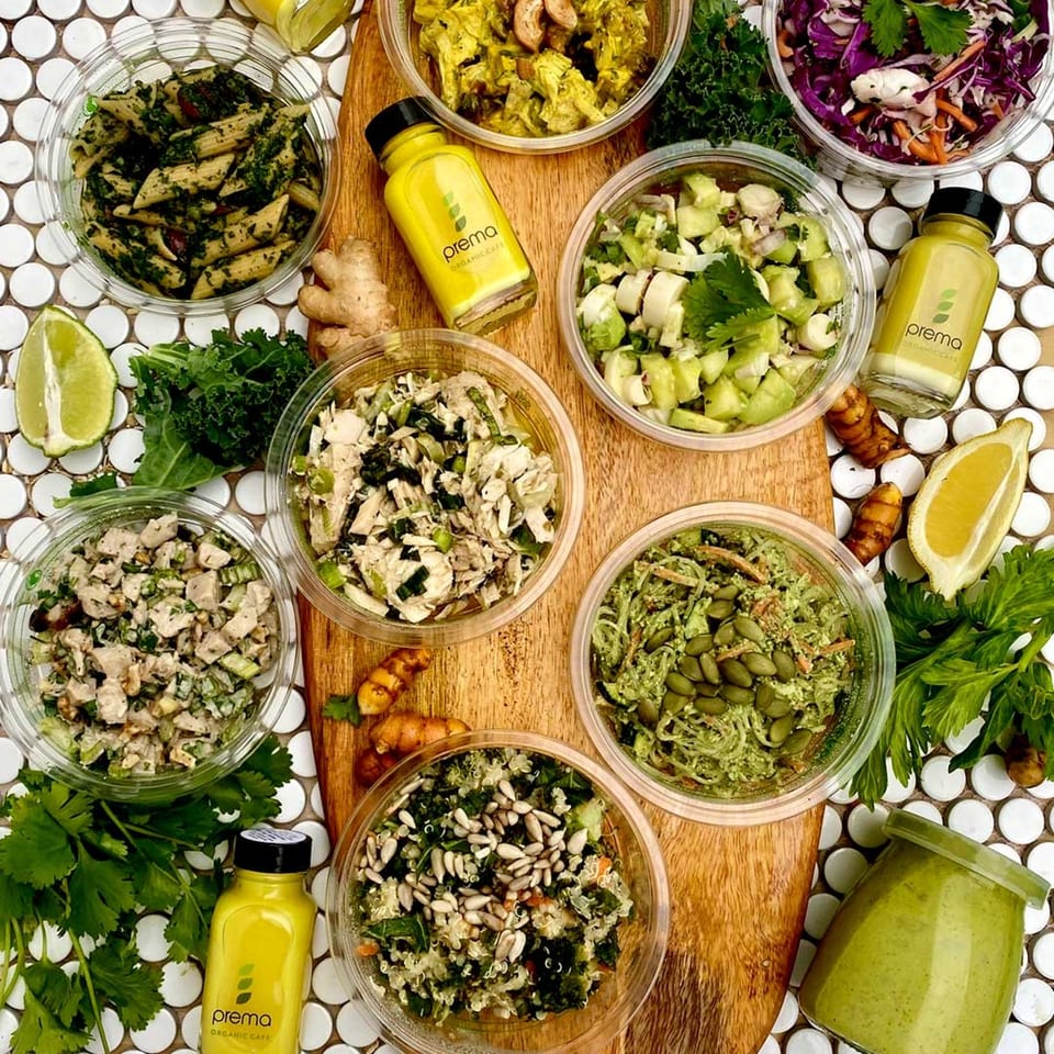 An overhead view of various Prema Organic Cafe salads, pasta, and drinks on a wooden board.