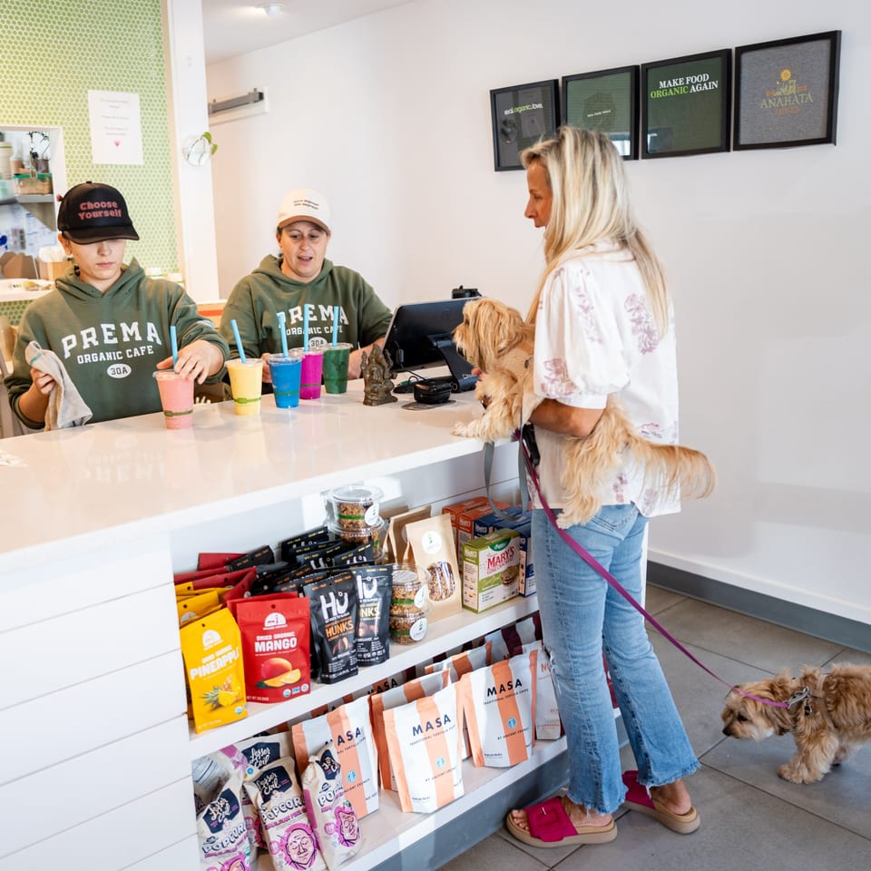 Customers and their dogs at the counter of Prema Organic Cafe, with colorful smoothies and snacks.