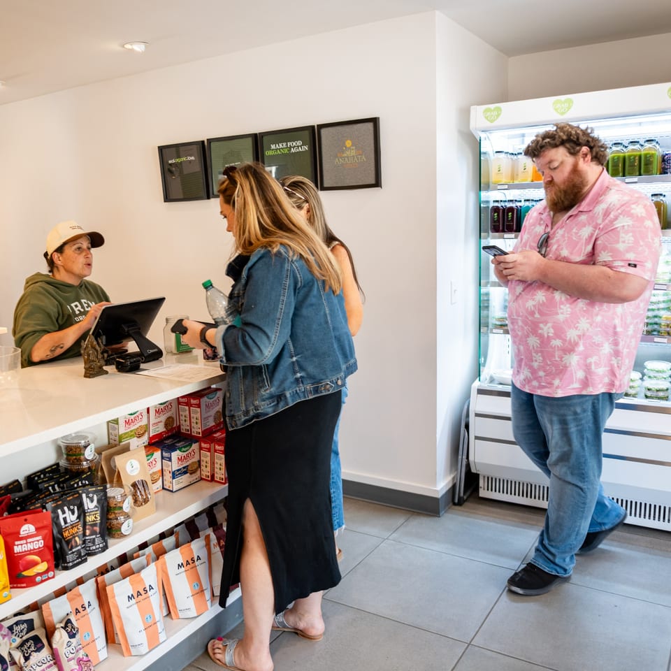 Customers interact with a cashier and browse products in a bright, modern health food store.