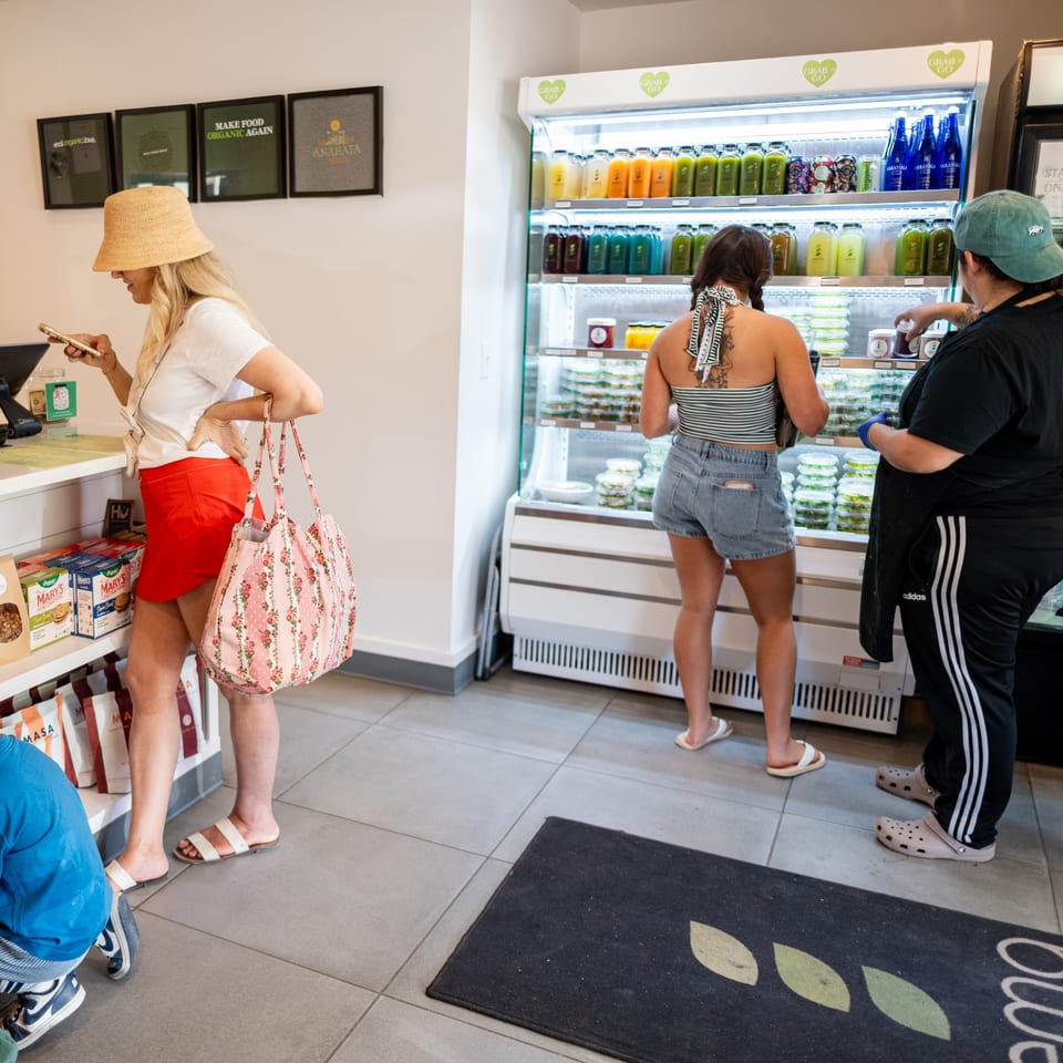 Customers browse a refrigerated display of juices and prepared foods in a bright, modern organic market.