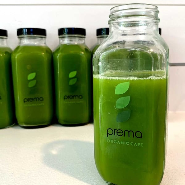Several glass bottles of green juice with "prema ORGANIC CAFE" labels on a white surface.