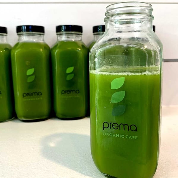 Several glass bottles of green juice from Prema Organic Cafe, with one in the foreground.