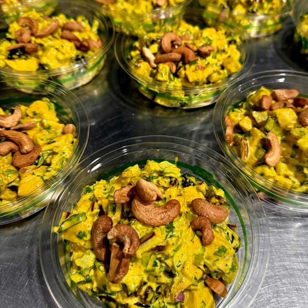 Multiple clear plastic containers filled with yellow curry chicken salad topped with cashews.