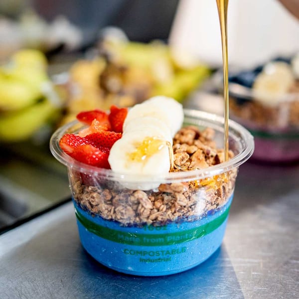 Honey drizzles over a blue smoothie bowl topped with granola, strawberries, and banana slices.